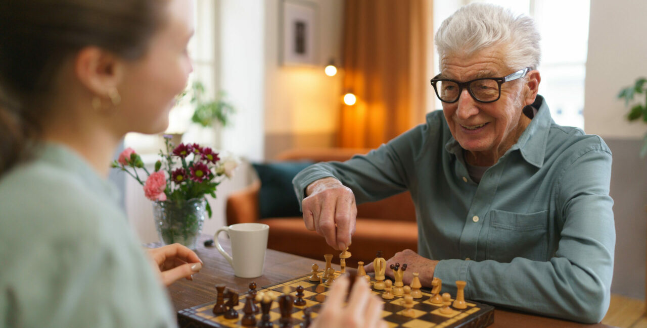 Senior man playing chess with his granddaughter.